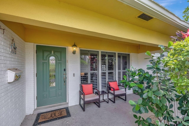 doorway to property featuring covered porch and brick siding