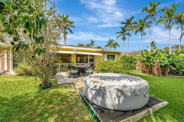 back of property with stucco siding, a hot tub, a yard, and a patio