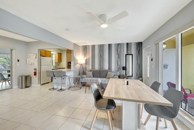 dining room with wallpapered walls, a ceiling fan, baseboards, and light tile patterned floors