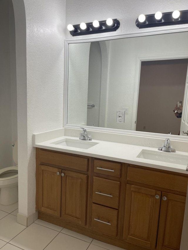 full bath with a sink, toilet, double vanity, and tile patterned floors