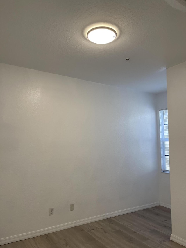 empty room featuring wood finished floors, baseboards, and a textured ceiling