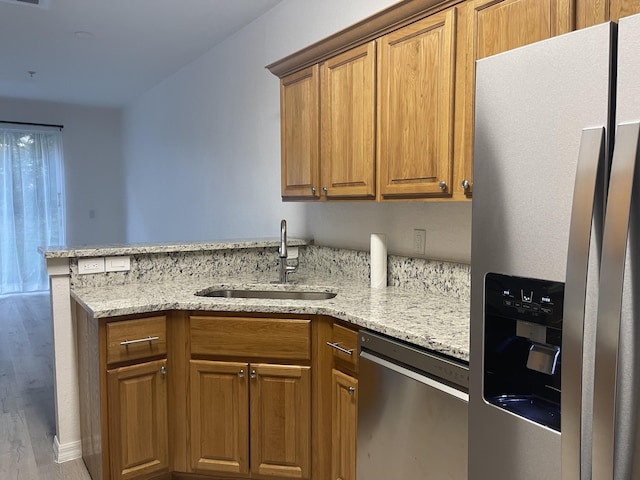 kitchen featuring light stone countertops, a peninsula, a sink, appliances with stainless steel finishes, and brown cabinets