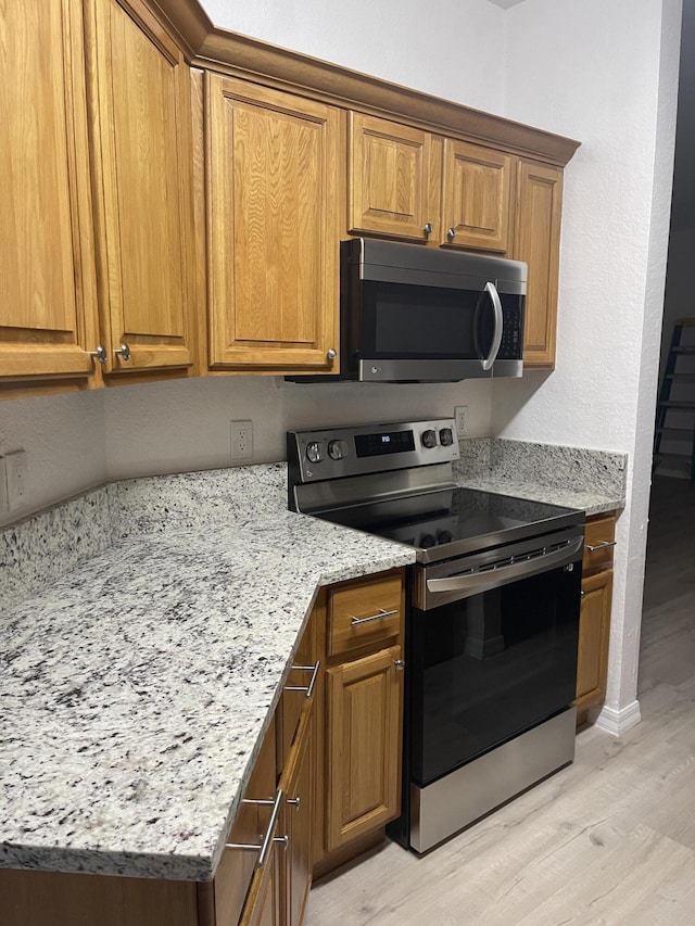 kitchen featuring light stone counters, brown cabinets, stainless steel appliances, and light wood-type flooring