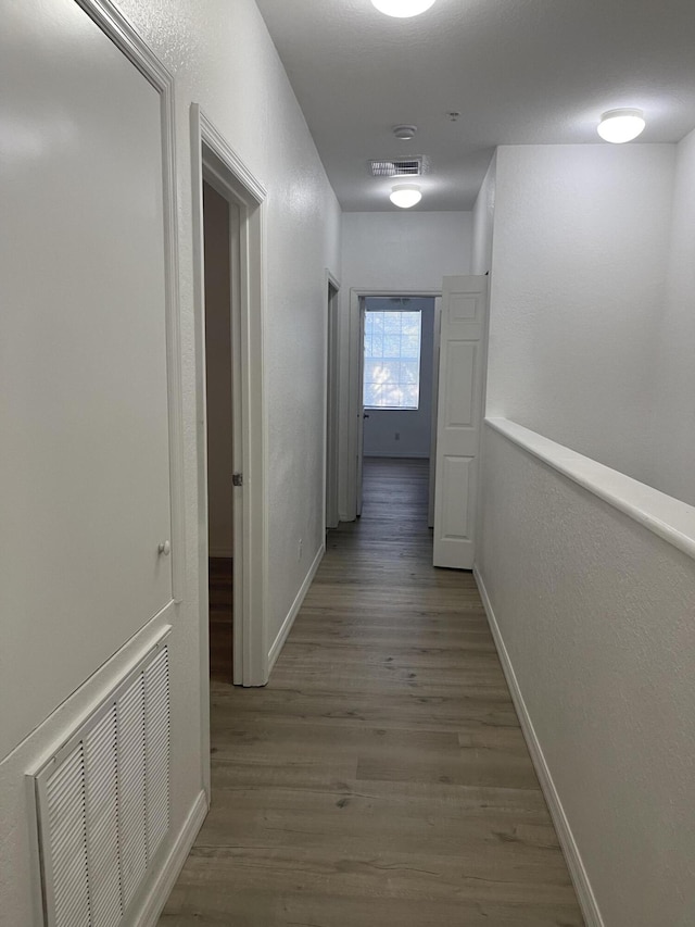 hallway featuring visible vents, baseboards, and wood finished floors