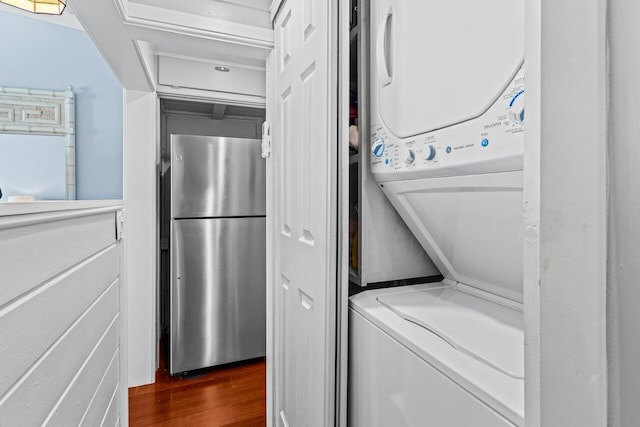 clothes washing area featuring laundry area, stacked washer and dryer, and dark wood-style floors