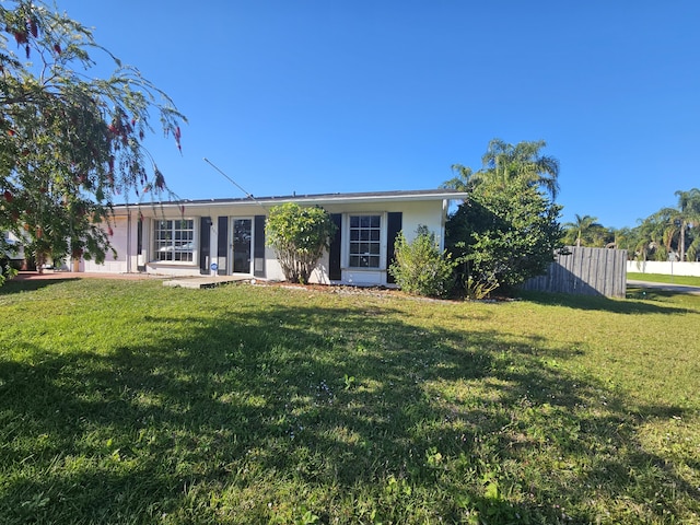 rear view of property with stucco siding, a yard, and fence