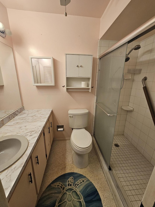 full bathroom featuring speckled floor, vanity, a shower stall, and toilet