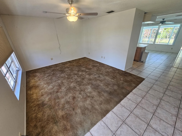 empty room with light tile patterned floors, visible vents, light colored carpet, and ceiling fan