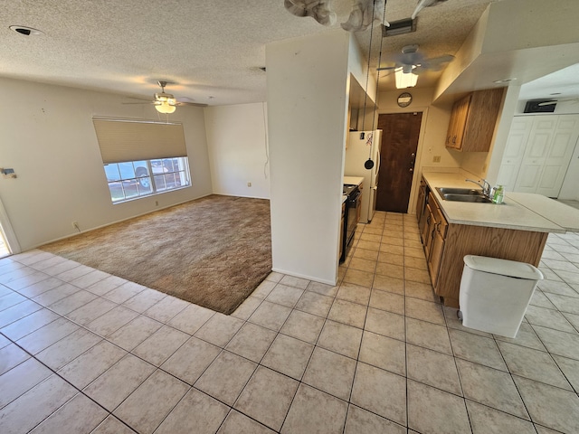 kitchen featuring freestanding refrigerator, a sink, light countertops, light colored carpet, and brown cabinets