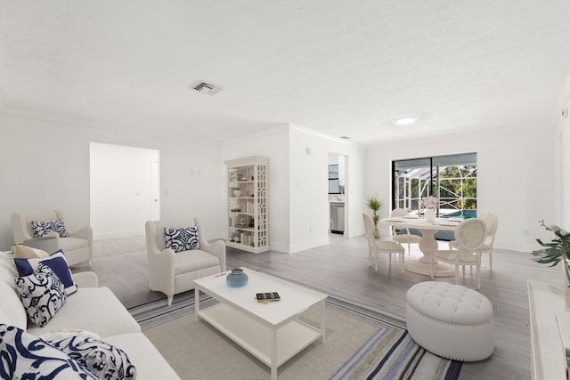 living area with visible vents, ornamental molding, a textured ceiling, wood finished floors, and baseboards