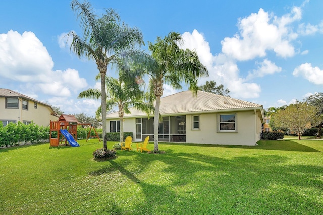 back of property with a tile roof, a playground, a lawn, and a sunroom