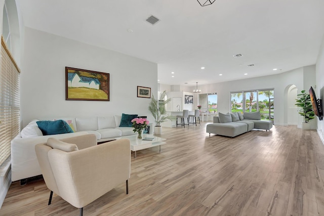 living room featuring recessed lighting, visible vents, light wood-style flooring, and arched walkways