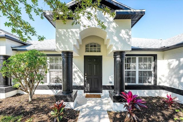 entrance to property with stucco siding and roof with shingles