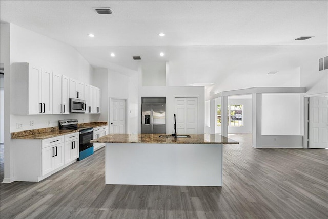 kitchen with high vaulted ceiling, an island with sink, a sink, dark stone countertops, and appliances with stainless steel finishes