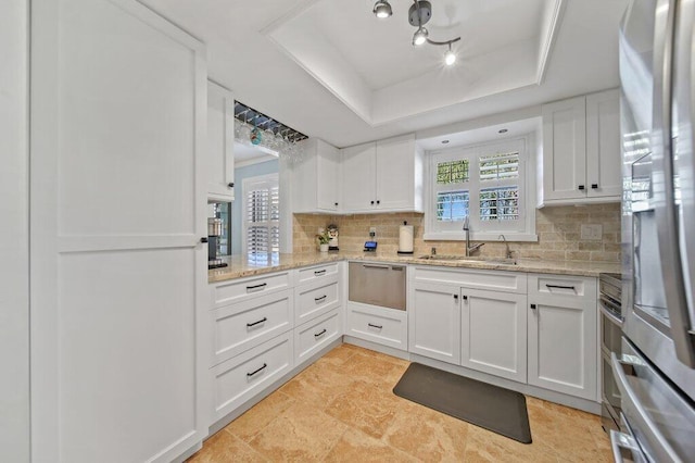 kitchen featuring a tray ceiling, appliances with stainless steel finishes, white cabinets, a warming drawer, and a sink