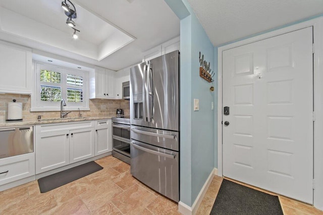 kitchen featuring baseboards, a sink, white cabinets, appliances with stainless steel finishes, and tasteful backsplash