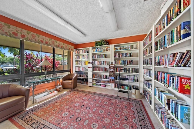 sitting room featuring tile patterned flooring, wall of books, and a textured ceiling