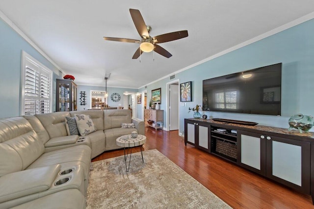 living room with a ceiling fan, baseboards, wood finished floors, visible vents, and ornamental molding