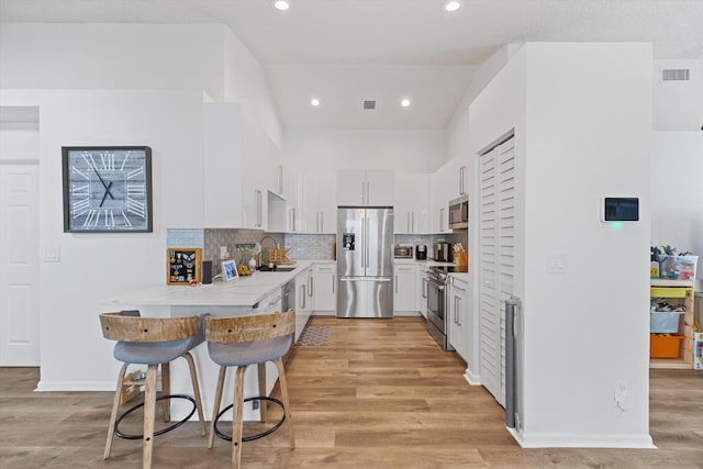 kitchen with a sink, stainless steel appliances, light countertops, light wood-style floors, and backsplash