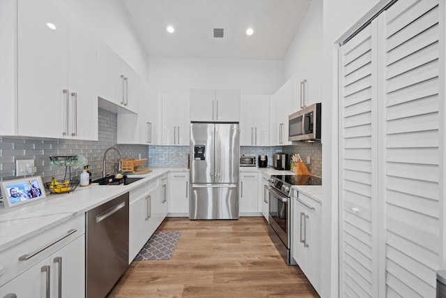 kitchen featuring visible vents, light wood-style flooring, white cabinets, stainless steel appliances, and a sink