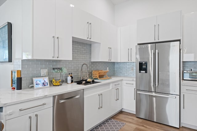 kitchen with tasteful backsplash, light wood-style flooring, appliances with stainless steel finishes, white cabinets, and a sink