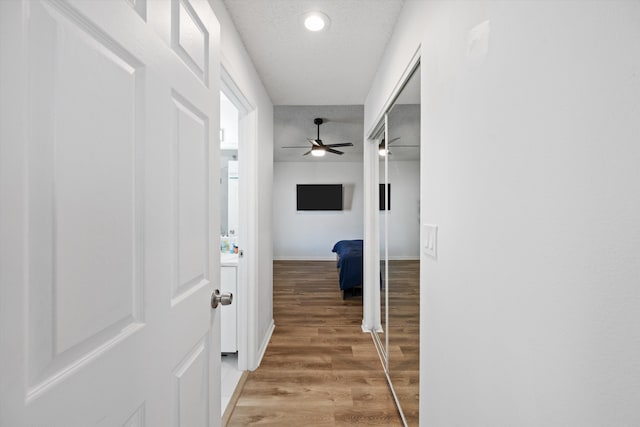 hallway with baseboards, light wood finished floors, and a textured ceiling