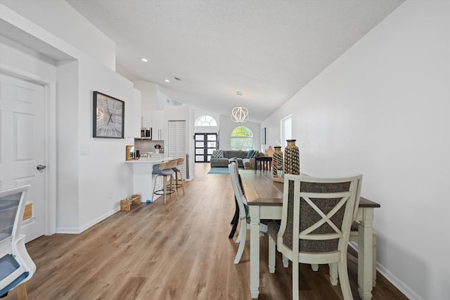 dining room featuring baseboards, lofted ceiling, an inviting chandelier, and light wood finished floors