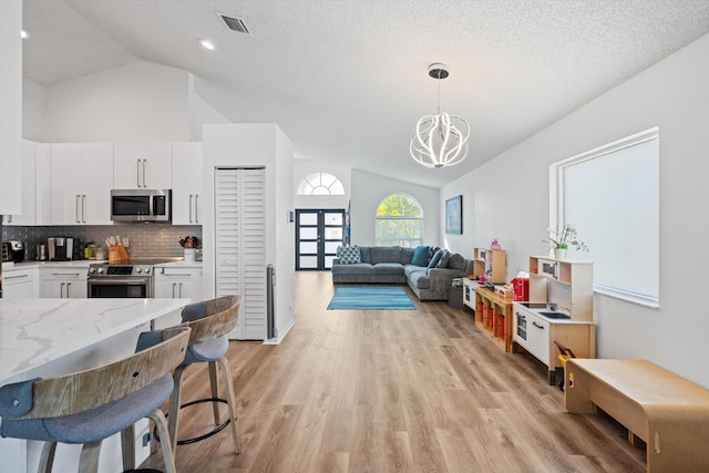 kitchen with visible vents, light wood finished floors, vaulted ceiling, appliances with stainless steel finishes, and backsplash