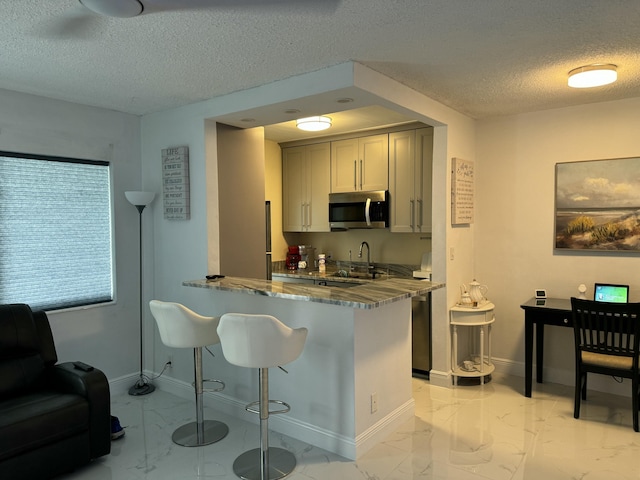 kitchen with stainless steel microwave, marble finish floor, a peninsula, and a sink