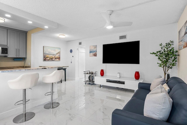 living room with visible vents, marble finish floor, a textured ceiling, baseboards, and ceiling fan