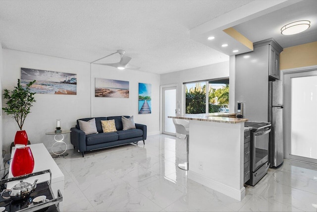 kitchen with a kitchen bar, marble finish floor, a textured ceiling, stainless steel appliances, and light stone countertops