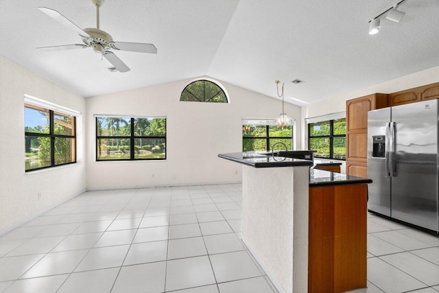 kitchen featuring light tile patterned floors, lofted ceiling, an island with sink, stainless steel refrigerator with ice dispenser, and dark countertops