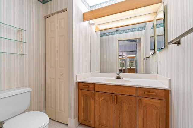 bathroom with wallpapered walls, toilet, vanity, and a closet