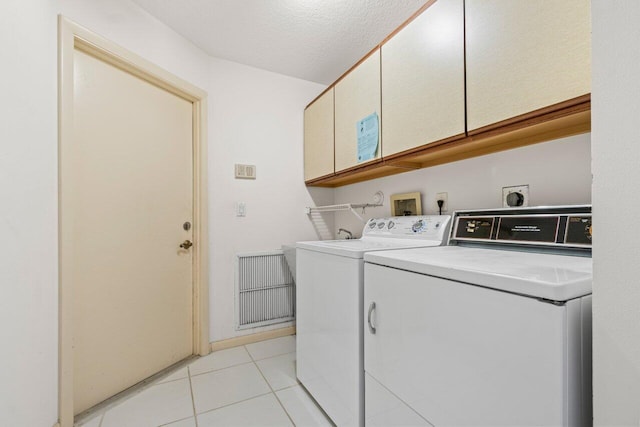 washroom with a textured ceiling, light tile patterned floors, cabinet space, and washer and clothes dryer