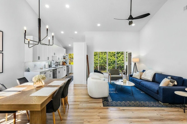 living area featuring ceiling fan with notable chandelier, light wood-type flooring, and high vaulted ceiling