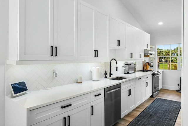 kitchen with light wood finished floors, a sink, under cabinet range hood, appliances with stainless steel finishes, and tasteful backsplash