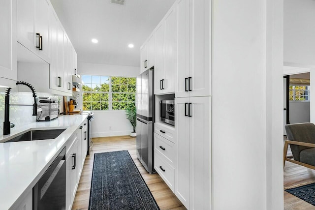 kitchen featuring a sink, light wood-style floors, appliances with stainless steel finishes, and white cabinets