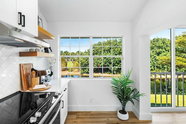 kitchen with range with electric cooktop, under cabinet range hood, open shelves, light wood finished floors, and decorative backsplash