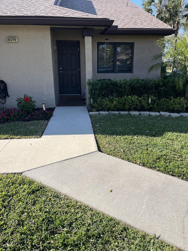 view of exterior entry featuring stucco siding and a shingled roof