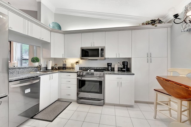 kitchen featuring dark stone counters, a sink, ornamental molding, vaulted ceiling, and stainless steel appliances