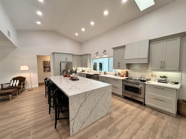 kitchen with a kitchen island, custom range hood, gray cabinets, a kitchen breakfast bar, and appliances with stainless steel finishes