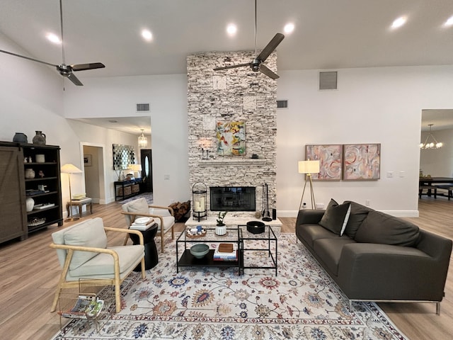 living room featuring a stone fireplace, ceiling fan with notable chandelier, visible vents, and wood finished floors