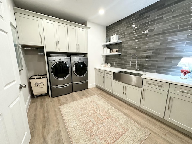 washroom featuring light wood finished floors, a sink, baseboards, cabinet space, and separate washer and dryer