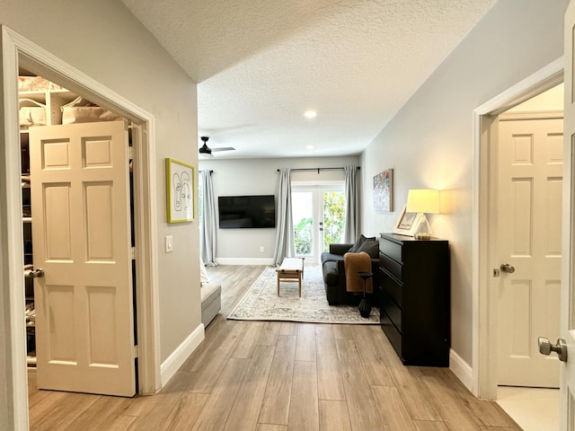 hallway featuring light wood-style floors, baseboards, and a textured ceiling