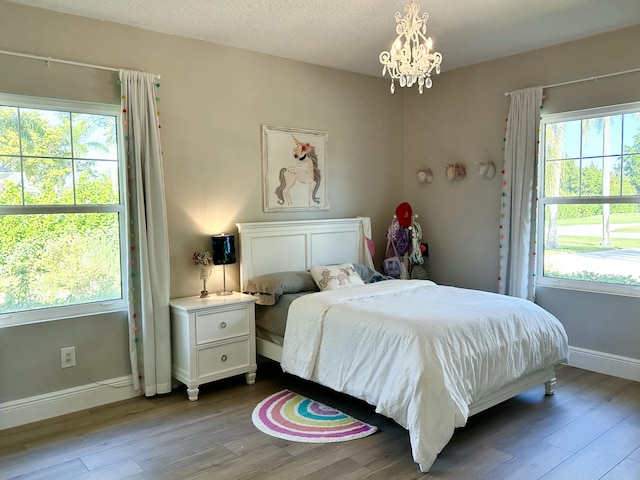 bedroom featuring multiple windows, an inviting chandelier, baseboards, and wood finished floors