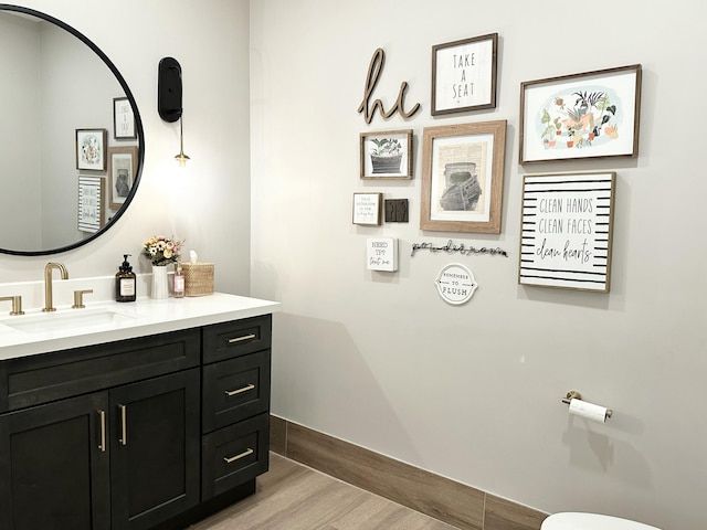 half bath featuring baseboards, wood finished floors, and vanity