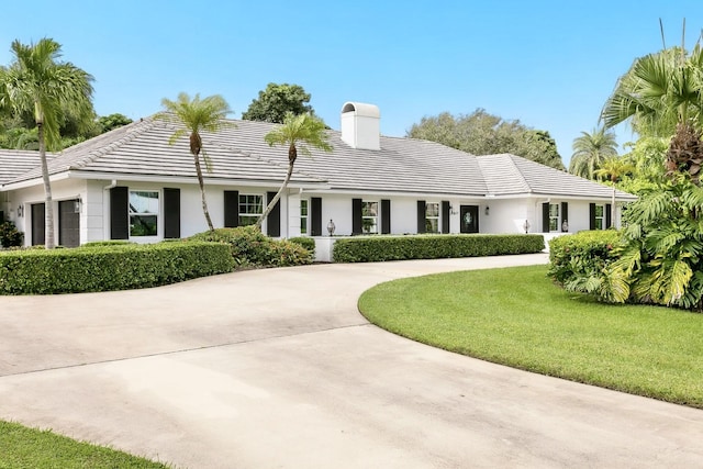 single story home with a chimney, concrete driveway, a front lawn, and a tile roof