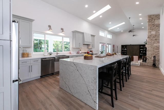 kitchen with light stone countertops, high vaulted ceiling, gray cabinetry, a large island, and stainless steel dishwasher