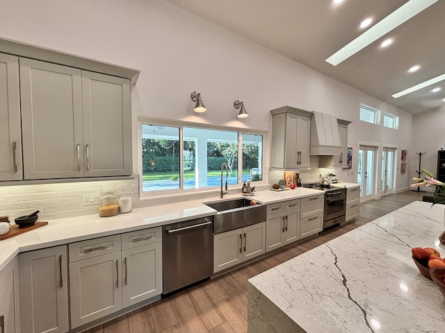 kitchen featuring a skylight, a sink, gray cabinetry, stainless steel dishwasher, and high quality stove