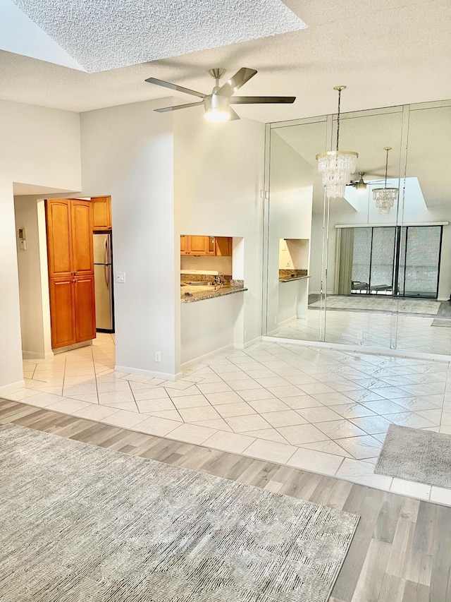 unfurnished room featuring high vaulted ceiling, ceiling fan with notable chandelier, a textured ceiling, light wood finished floors, and baseboards